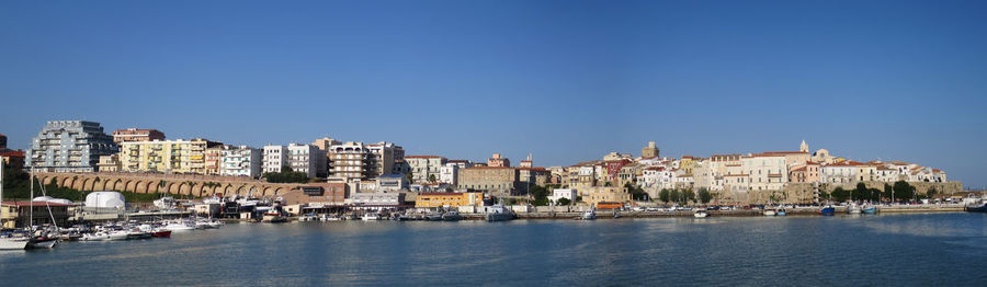 Buildings by sea against clear blue sky