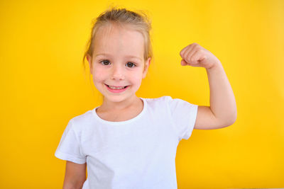 Portrait of young woman with arms raised standing against yellow background