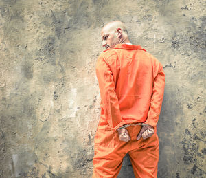 Rear view of man with handcuffs standing against wall