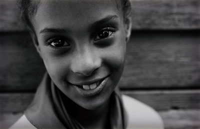 Close-up portrait of smiling girl against wooden wall