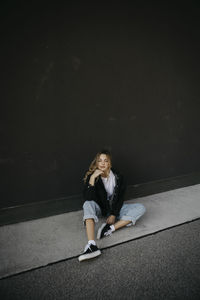 Young woman with hand on chin sitting against wall