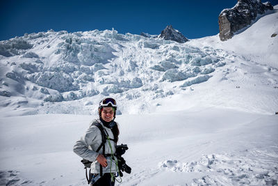 Full length portrait of smiling man standing on snowcapped mountain