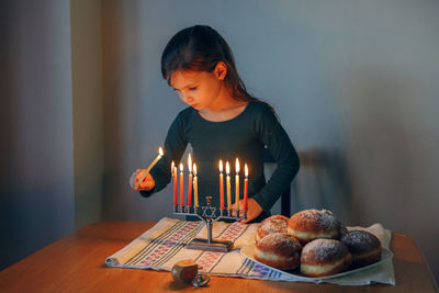 Cute girl holding burning candle by table