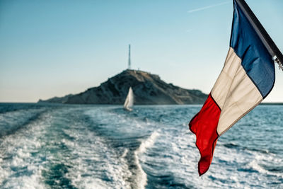 Flag hanging over sea against sky