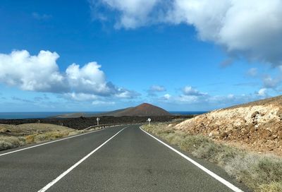 Empty road by mountains against sky