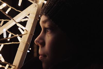 Close-up of boy by illuminated string light at night