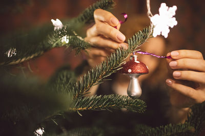 Cropped hands of woman tying decoration on christmas tree