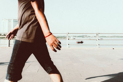 Low section of man standing by water against clear sky