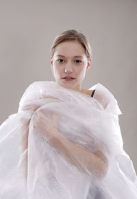 Portrait of woman wrapped in plastic against gray background