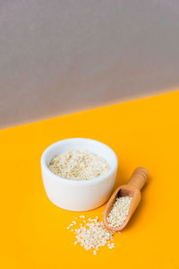 Wooden spoon with sesame seeds lies in a white mortar on a yellow background. healthy eating. keto 