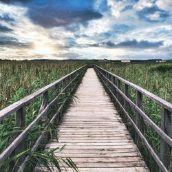 Wooden footbridge on field against sky