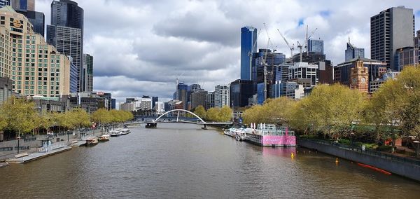 Bridge over river amidst buildings in city against sky