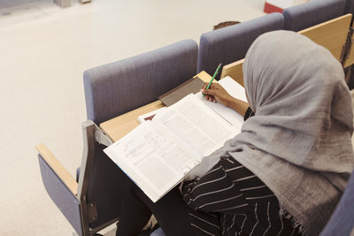 High angle view of student in hijab studying from book at lecture hall in university
