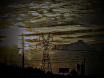 Low angle view of electricity pylon against cloudy sky