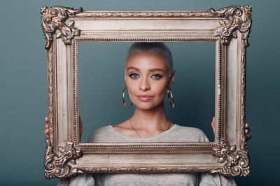 Portrait of young woman with picture frame against colored background