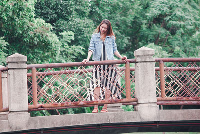 Portrait of woman standing by railing against trees