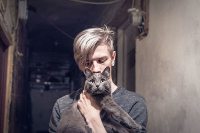 Young woman with short hair carrying cat while standing at home