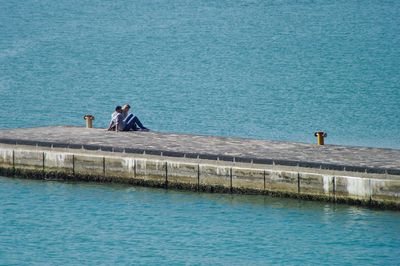 Couple sitting on pier at sea