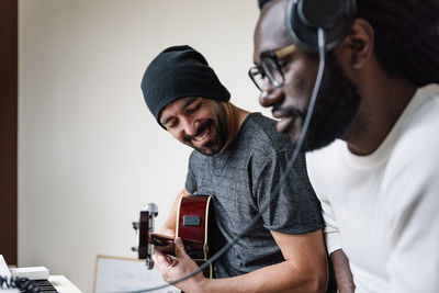 Man playing guitar while friend listening through headphones