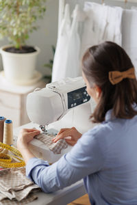 Rear view of woman works on sewing machine at workshop