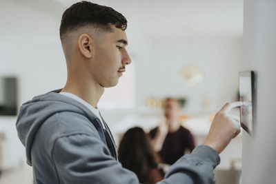 Side view of boy using home automation app through digital tablet mounted on wall