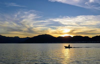 Silhouette person in lake against sky during sunset