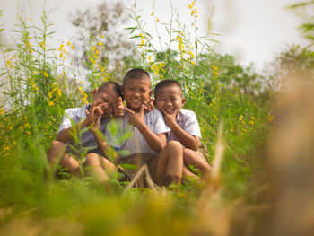 Portrait of smiling friends gesturing while sitting on field