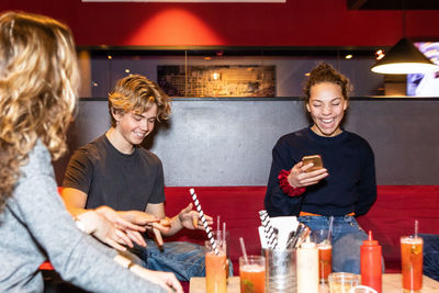 Cheerful multi-ethnic teenage friends enjoying while sitting on sofa at restaurant