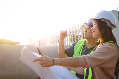 Side view of young woman looking at camera against sky