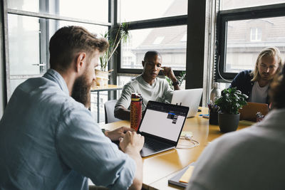 Businessman working on laptop by colleagues in tech-startup company