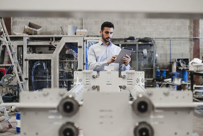 Businessman using tablet pc standing behind machine at industry