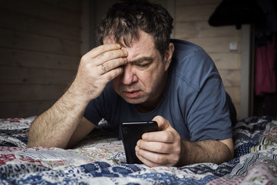 Midsection of man using mobile phone while sitting on bed at home