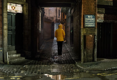 Rear view of man standing on wet street in city at night