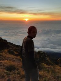 Side view of boy standing on landscape during sunset