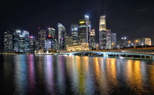 Illuminated buildings by river against sky at night