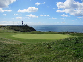 Golf course by sea against sky