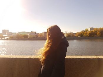Woman standing by river against sky in city