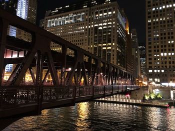 Bridge over river by illuminated buildings at night