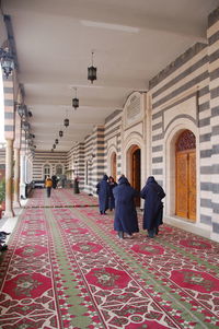 Rear view of people walking on tiled floor against building