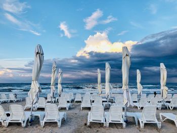 An empty beach with white sunbeds and umbrellas on a day with dark storm clouds