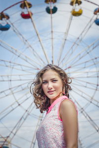 Portrait of smiling young woman standing against ferries wheel