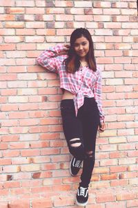 Portrait of young woman standing against brick wall