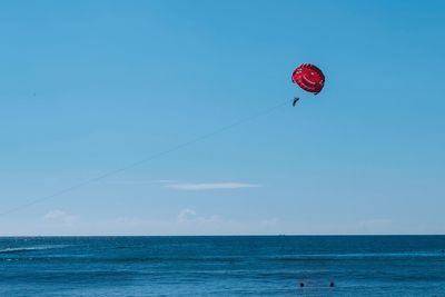 Low angle view of person parasailing over sea against blue sky