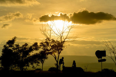 Silhouette people by tree against sky during sunset