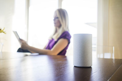 Smart home loudspeaker on table with woman using tablet in the background