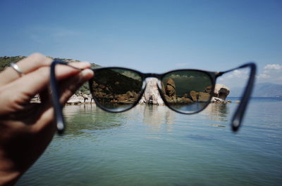 Midsection of person holding sunglasses against sky