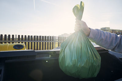 Man walking with rubbish. hand carrying plastic bag against garbage cans on street.