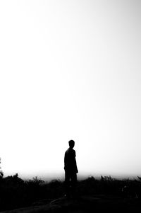 Rear view of silhouette man standing on field against clear sky