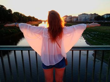 Rear view of woman standing by water at sunset