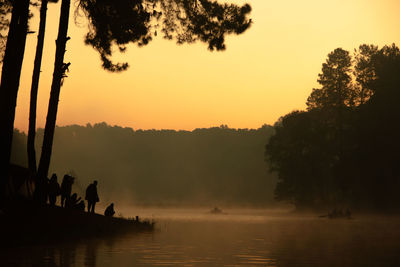 Silhouette trees by lake against sky during sunset